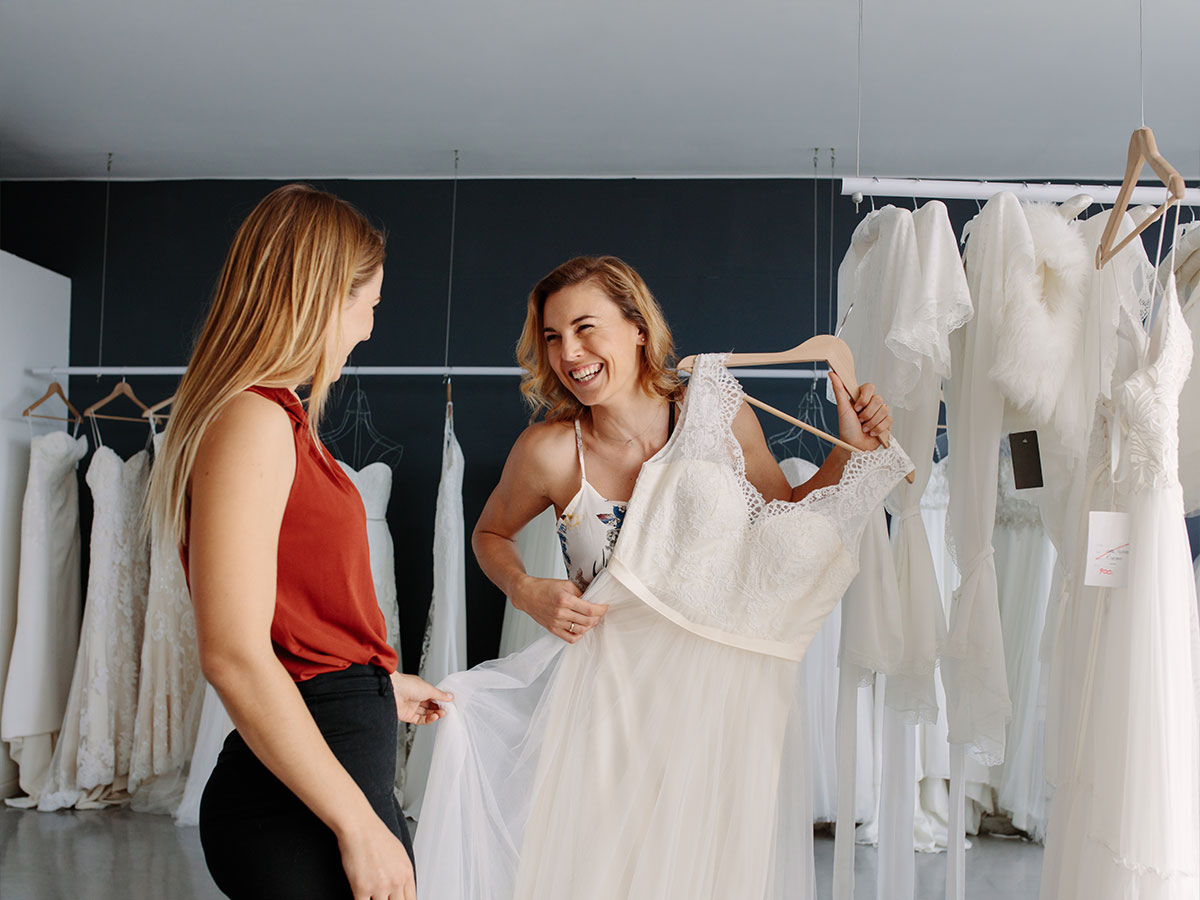 Two women holding up wedding dress inside dress shop