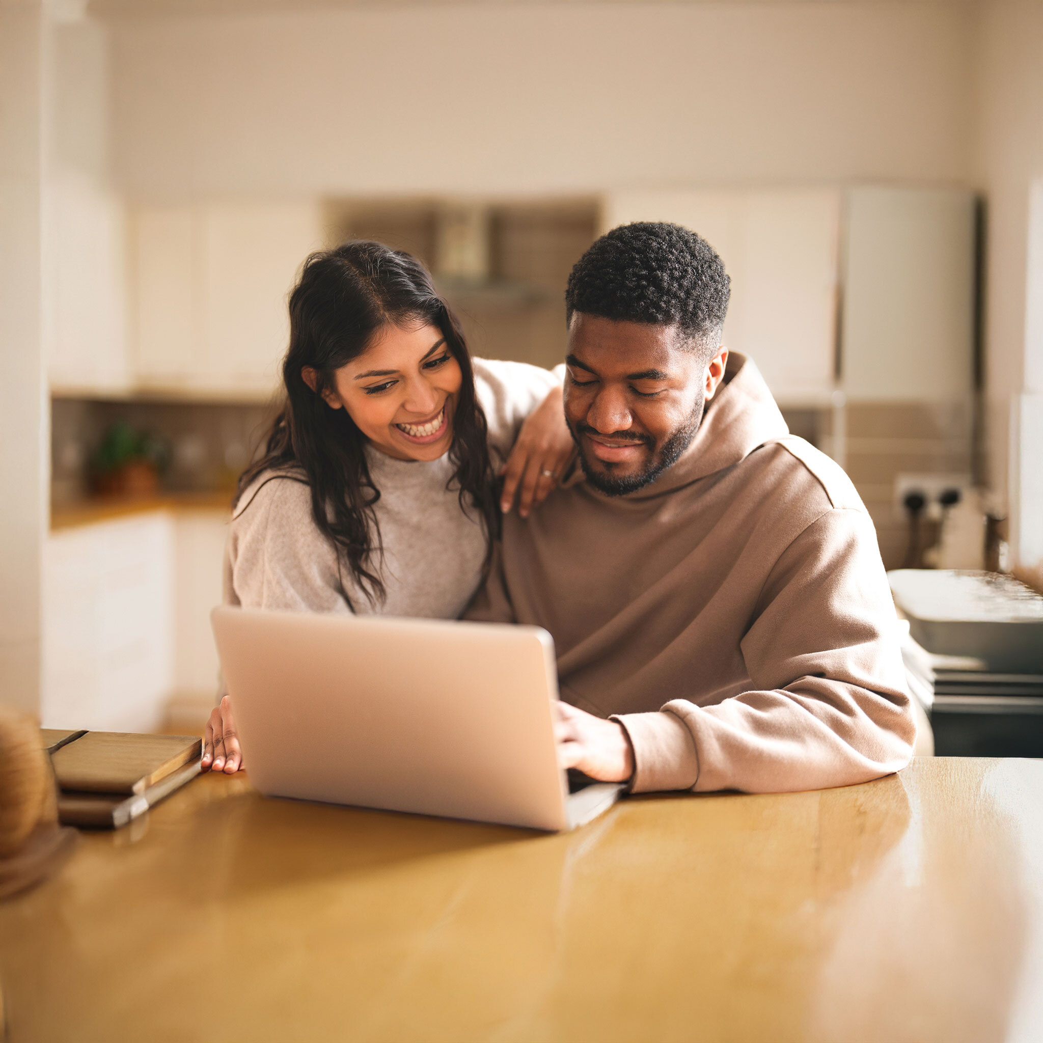 Smiling couple sitting at a kitchen table looking at a laptop