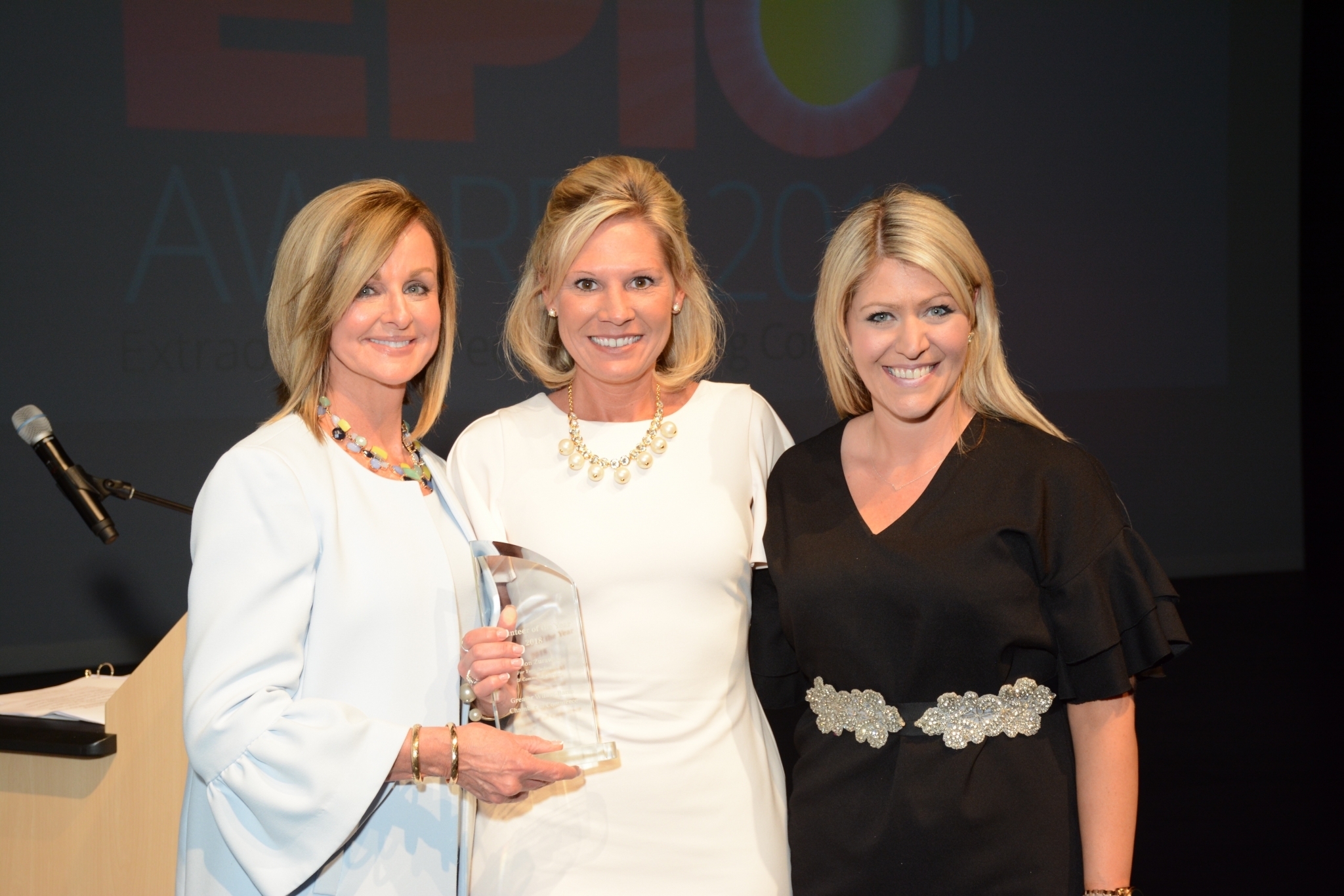 Three Women Smile While Holding an Award