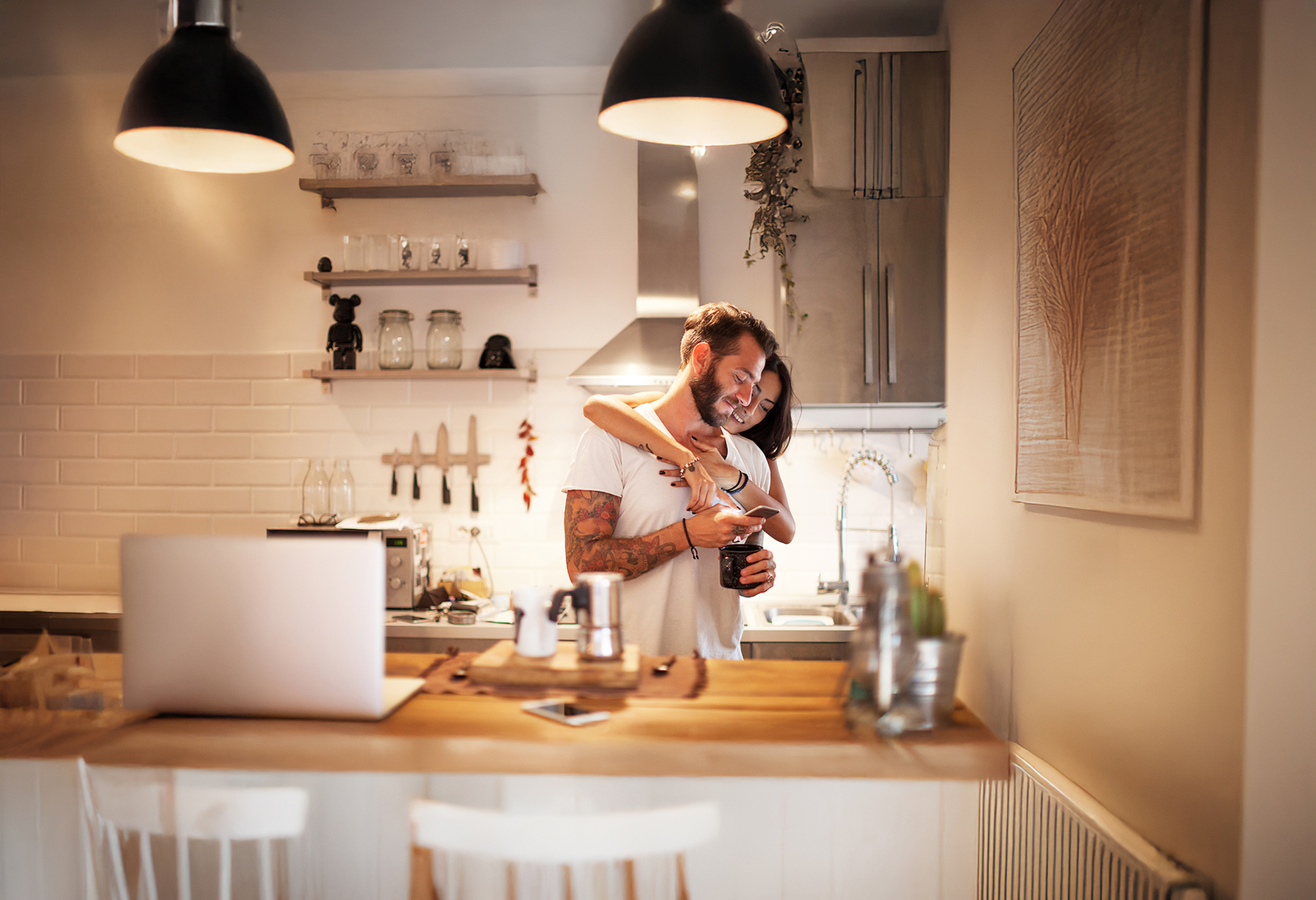 Two people embracing in a kitchen, looking at a mobile phone
